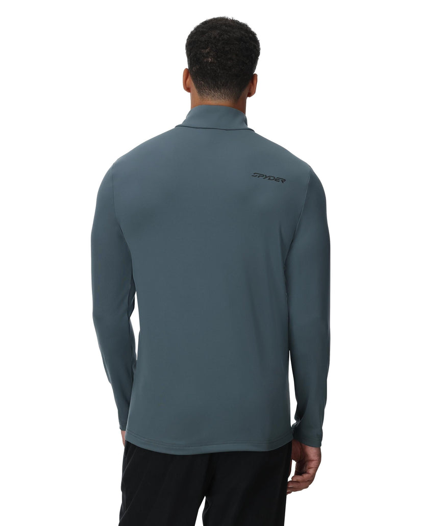 Person wearing a gray long-sleeve shirt with a brand logo on the back, standing against a white background