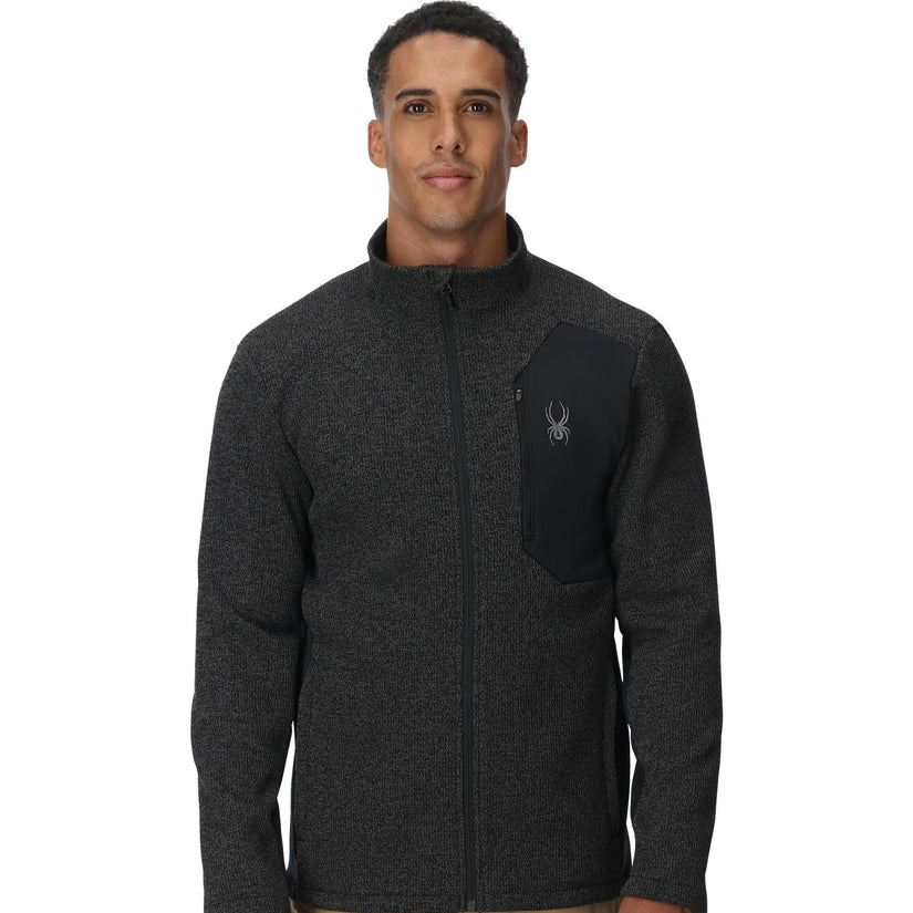 Man wearing a dark gray fleece jacket with a brand logo on a white background
