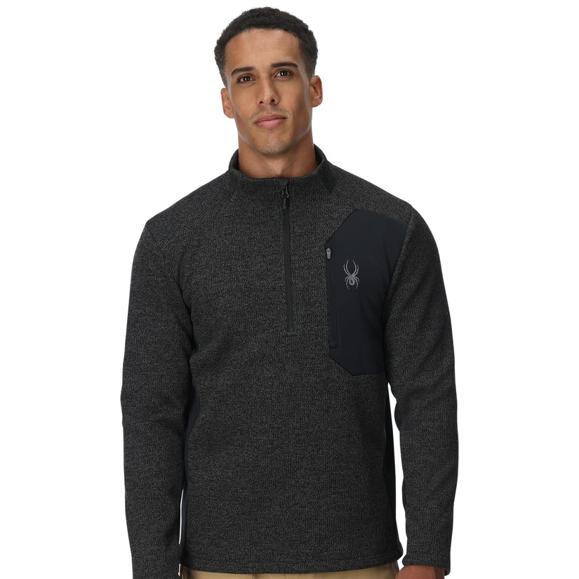 Man wearing a dark gray pullover with a logo on a white background