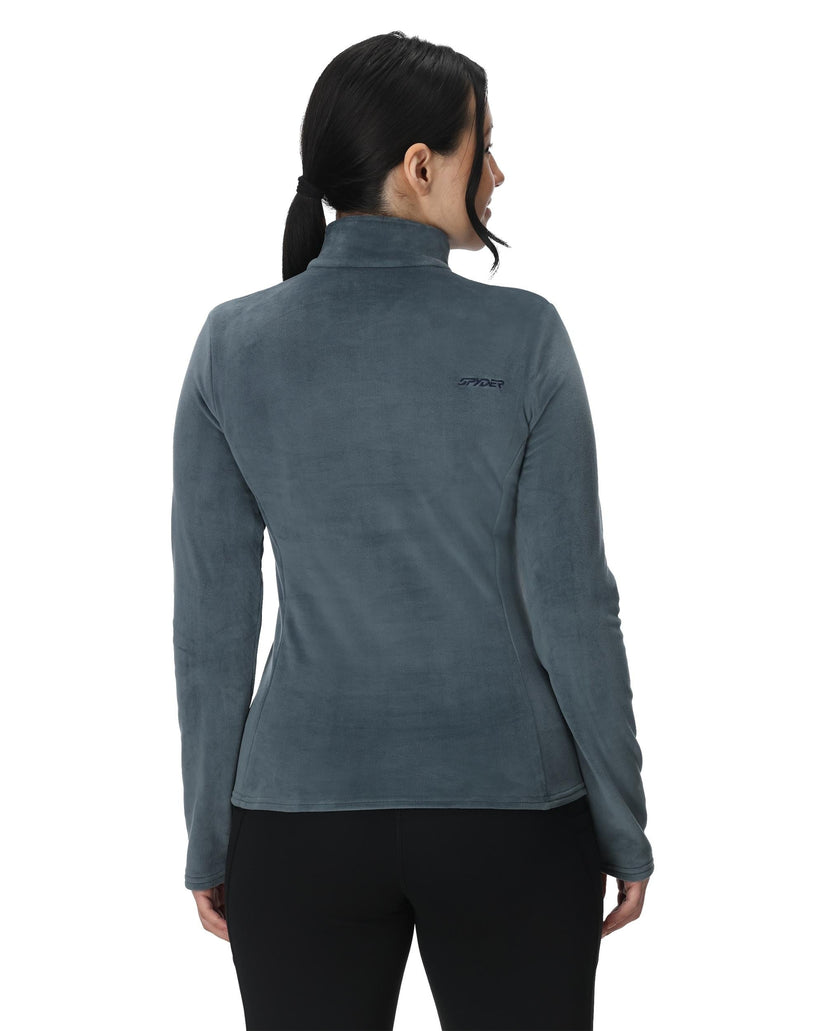 Woman wearing a gray fleece jacket with a visible brand logo on the back, standing against a white background.