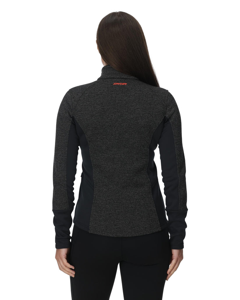 Person wearing a dark gray jacket with a brand logo on the back against a white background