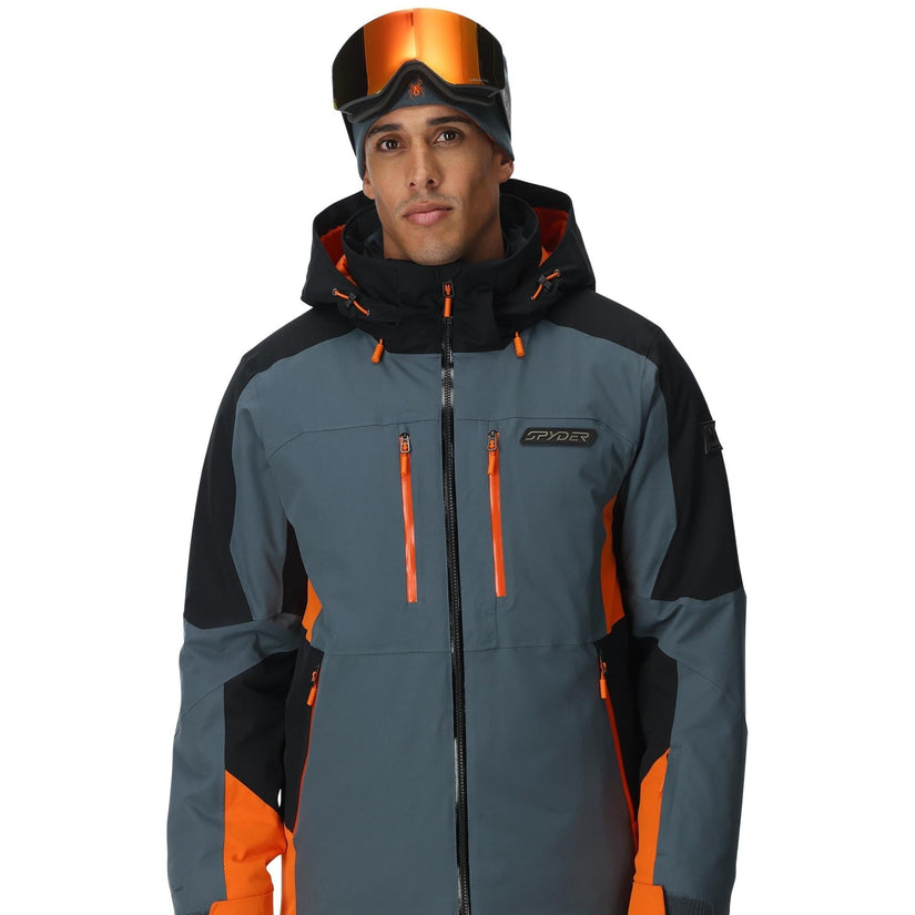 Person wearing a gray and orange ski jacket with goggles on a white background