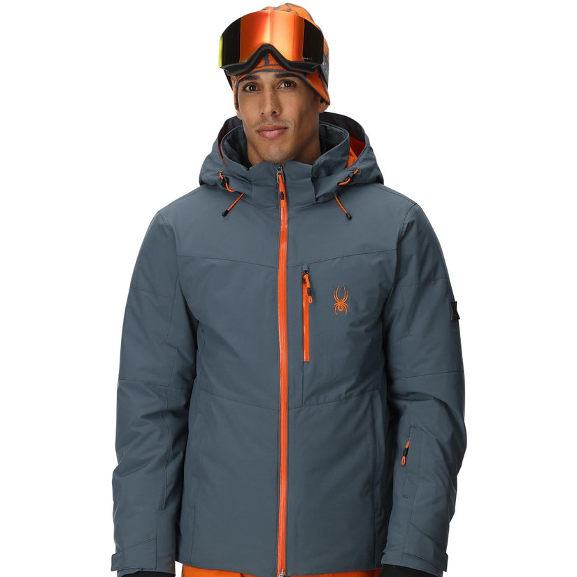 Person wearing a gray jacket with orange accents and orange ski pants on a white background