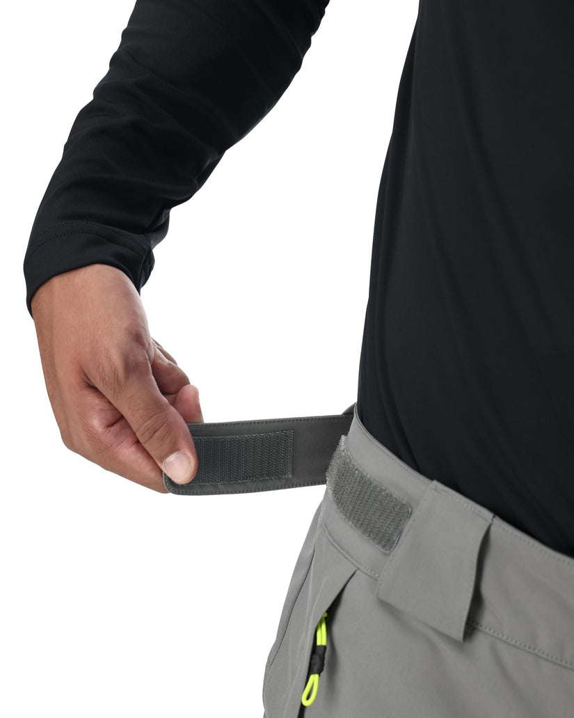 Person adjusting a black belt on gray pants against a white background