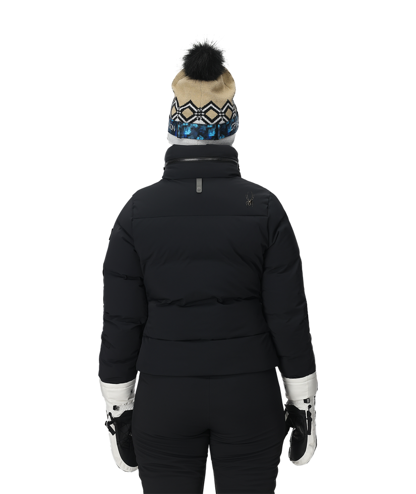 Person wearing a black puffer jacket, black pants, white gloves, and a patterned beanie on a white background