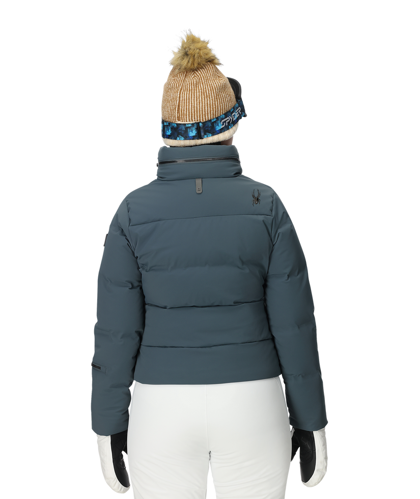 Person wearing a blue puffer jacket, white pants, and a beanie with a pom-pom on a white background