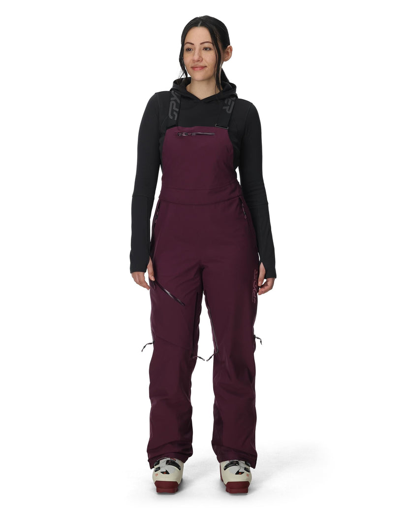Person wearing a maroon bib overalls and black long-sleeve shirt on a white background